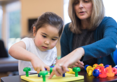 An occupational therapist works with a kindergarten-age ethnic girl on her coordination skills. She is showing her a fun exercise to practice putting pegs into a plastic board. pediatric occupational therapy