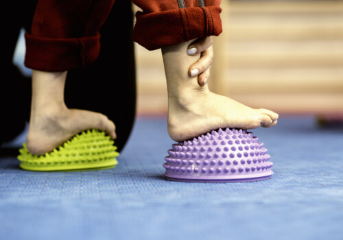 Flat Feet Corrective Exercises - Little boy walking over spikey half balance rubber balls on a physical therapy exercise class. Physical therapist helping pediatric physical therapy feet walking on cushions